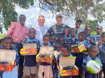 Lots of children holding boxes of donated shoes, sports kits and school uniform.