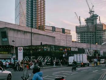 Box park, a large black bar with white stripes on it. There are grey buildings in the background.