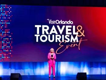 Visit Orlando Travel & Tourism Conference - woman speaking and announcing in a pink suit.