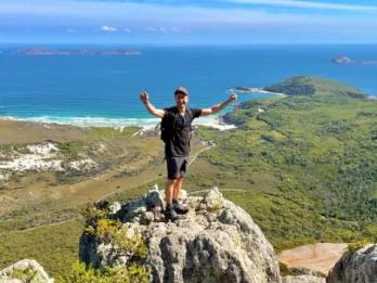 Wilsons Promontory Day Tour Happy man with arms raised, standing on a rock overlooking scenic views at Wilsons Promontory
