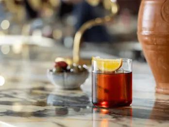 A clay vase next to a delicious drink on a bar top. The drink is a Negroni.