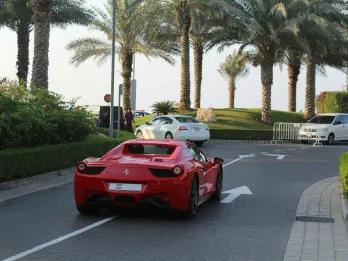 Ferrari driving on a road lined with palm trees next to regular cars.