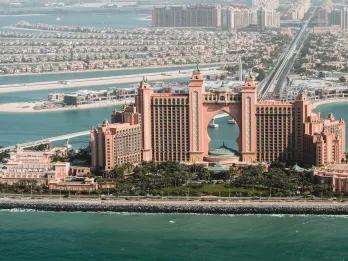 Large pink hotel with a huge hole in the middle at the end of a long road out into the sea with sand banks and building stemming from this road, forming a tree like shape.