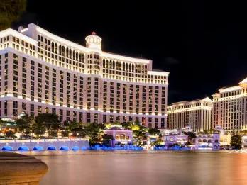 Bellagio Resort & Casino Tall white hotel with luxurious decor and a lake in front with fountains.