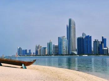White sand beach with a boat on it and there are tall buildings across the water from it.