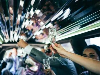 People in suits and dressed formally holding up glasses of champagne to cheers inside of a limo.