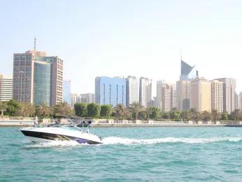 Speed boat travelling through the sea at high speeds past a beach and many modern buidlings.