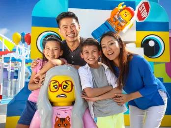 Family of four posing with a cat lady lego statue in front of huge lego blocks and characters.