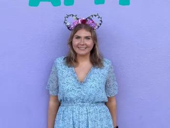 Meet Amy A girl stood in customised mickey ear headbands in front of a large purple wall and large writing above her head saying AMY.
