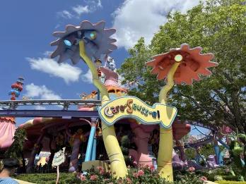 A sign that says Caro-Seuss-el, with large flower statues and the background there's an undercover carousel.