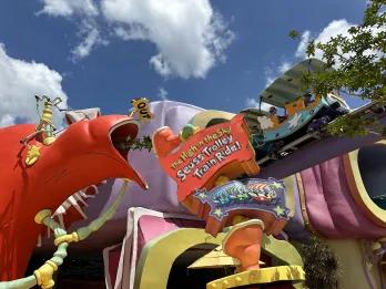 The High in the Sky Seuss Trolley Train Ride Multi coloured cartoon land with giant fish statues and a high up train track with a cartoon train going along the track.