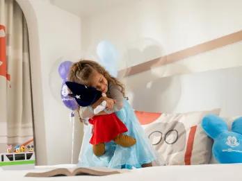 A young girl hugging a Mickey Mouse plush on an Incredibles themed bed