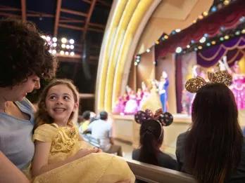 A girl in a Belle costume smiling while watching a Beauty and the Beast stage show