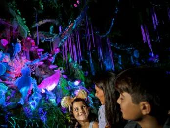 A mum and two children on an Avatar themed boat ride through a bioluminescent forest