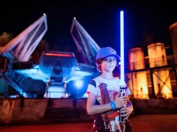 A young boy holding a light saber in front of an X Wing ship