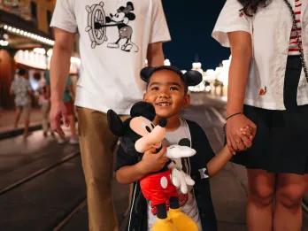 A young boy with a Mickey Mouse plush holding hands with a woman on Main Street