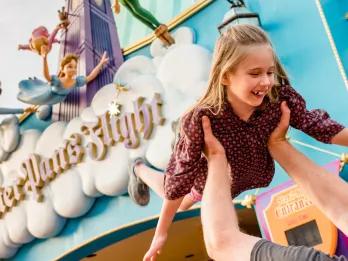 A young girl being held up in front of the entrance to Peter Pan's Flight