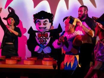 LEGOLAND Dubai Halloween Dracula lego character danging by lego dj deck with kids gethered around wearing halloween costumes.