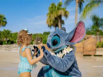 An adorable character meet-and-greet at a sunny Walt Disney World location, showing a young child playing with Stitch on the beach, a great example of fun outside the main theme parks for young families.