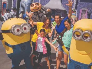 A joyful family with two young kids raising their hands in excitement while meeting the Minions and Gru at Universal Studios Florida, highlighting an essential Universal Orlando Resort experience.
