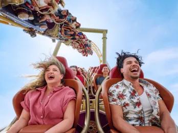 Two adults laughing and screaming with their hair flying while riding a high-speed roller coaster at Universal Orlando Resort, illustrating the kind of thrill ride experience you secure by booking tickets in advance.