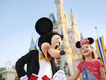 Mickey Mouse and a young girl smiling outside the castle at Walt Disney World in Orlando