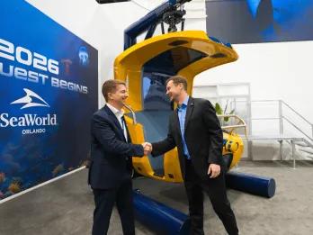 Two men shaking hands in front of the ride vehicle, a yellow hanging seat.