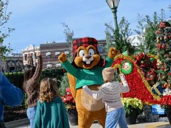 Children waving at a friendly squirrel character, surrounded by Christmas decorations and red poinsettias, capturing a joyful holiday season moment and a memorable experience in Orlando.
