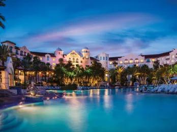 Illuminated lagoon-style swimming pool and tropical architecture at a premium Universal Orlando Resort hotel at night.