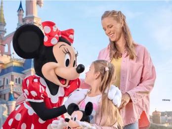 A young girl and her mother smiling with the Minnie Mouse character in front of Sleeping Beauty Castle at Disneyland Paris.