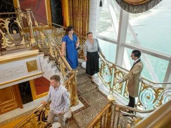 Guests on the Burj Al Arab Inside Tour walking down the luxurious gold staircase with an attendant, showcasing the opulent interior and expansive ocean view.