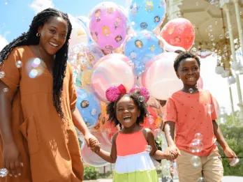 A joyful family surrounded by colorful Disney-themed balloons and bubbles at Walt Disney World