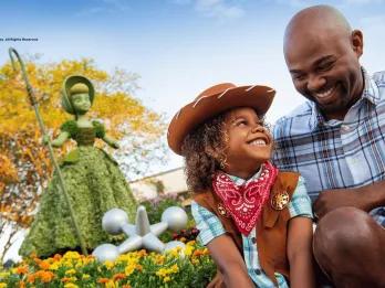 A young boy dressed as a cowboy smiling up at his dad, sat in front of a Bo Peep topiary