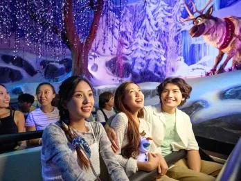Three adults sat on a boat ride through Frozen movie settings holding Olaf plush toys.