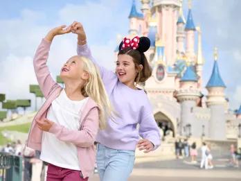 Two kids playing in front of the Disneyland Paris, one wearing a Minnie ear headband.