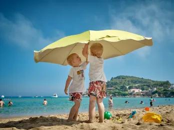 Children playing with beach umbrella on family summer vacation.