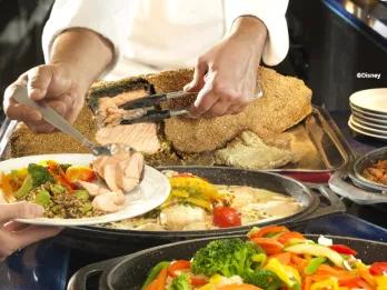 A chef serving fresh salt-crusted salmon and roasted vegetables at a Disneyland Paris buffet.