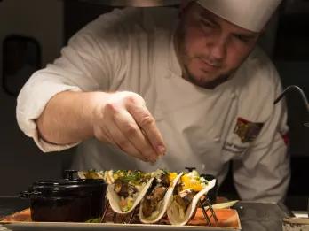 A chef garnishing fresh gourmet tacos on a platter at a Universal Orlando Resort restaurant.