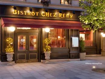 Exterior of Bistrot Chez Rémy at Disneyland Paris, featuring a charming Parisian bistro façade with warm glowing lights, decorative topiary and gold lettering at night