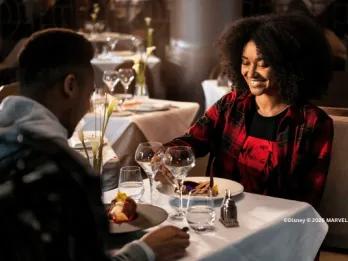 A couple enjoying a fine dining experience at Manhattan Restaurant in Disney Hotel New York, smiling over elegant plates and wine glasses in a sophisticated, softly lit setting