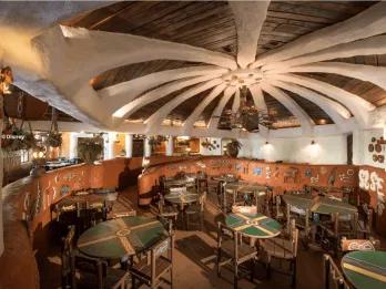 The vibrant interior of Restaurant Hakuna Matata at Disneyland Park, featuring a dramatic domed ceiling with white ribbed arches, colourful African-inspired murals, painted tribal tables and warm ambient lighting in an Adventureland setting