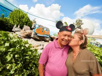 Couple wearing Mickey and Minnie ears near The Seas with Nemo & Friends pavilion at EPCOT, with Spaceship Earth in the background