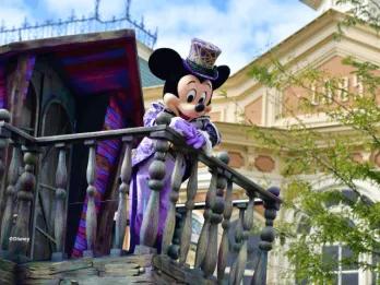 Mickey Mouse in a purple Halloween costume and top hat waving from a balcony at the Disney Halloween Festival