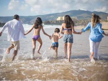 Family enjoying a summer beach holiday in Europe, running into the ocean together