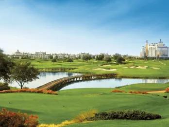 Golf course fairway with a footbridge over water and resort buildings at Reunion Resort