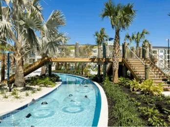 Lazy river winding through palm trees with a wooden bridge at Villatel Orlando Resort