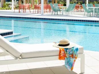 Sun lounger beside a swimming pool with a straw sun hat and colorful sarong