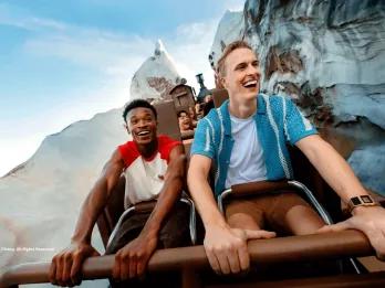 Two young men laughing as they ride the Expedition Everest roller coaster train through snow-covered mountain peaks