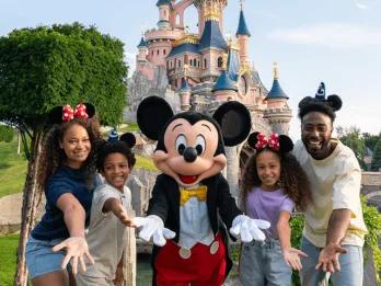 A family of four and Mickey Mouse pose happily in front of Sleeping Beauty Castle