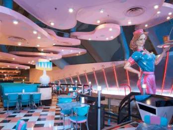 The retro 1950s-style interior of Annette's Diner, with checkerboard floors, teal booths, and a waitress statue at Disney Village